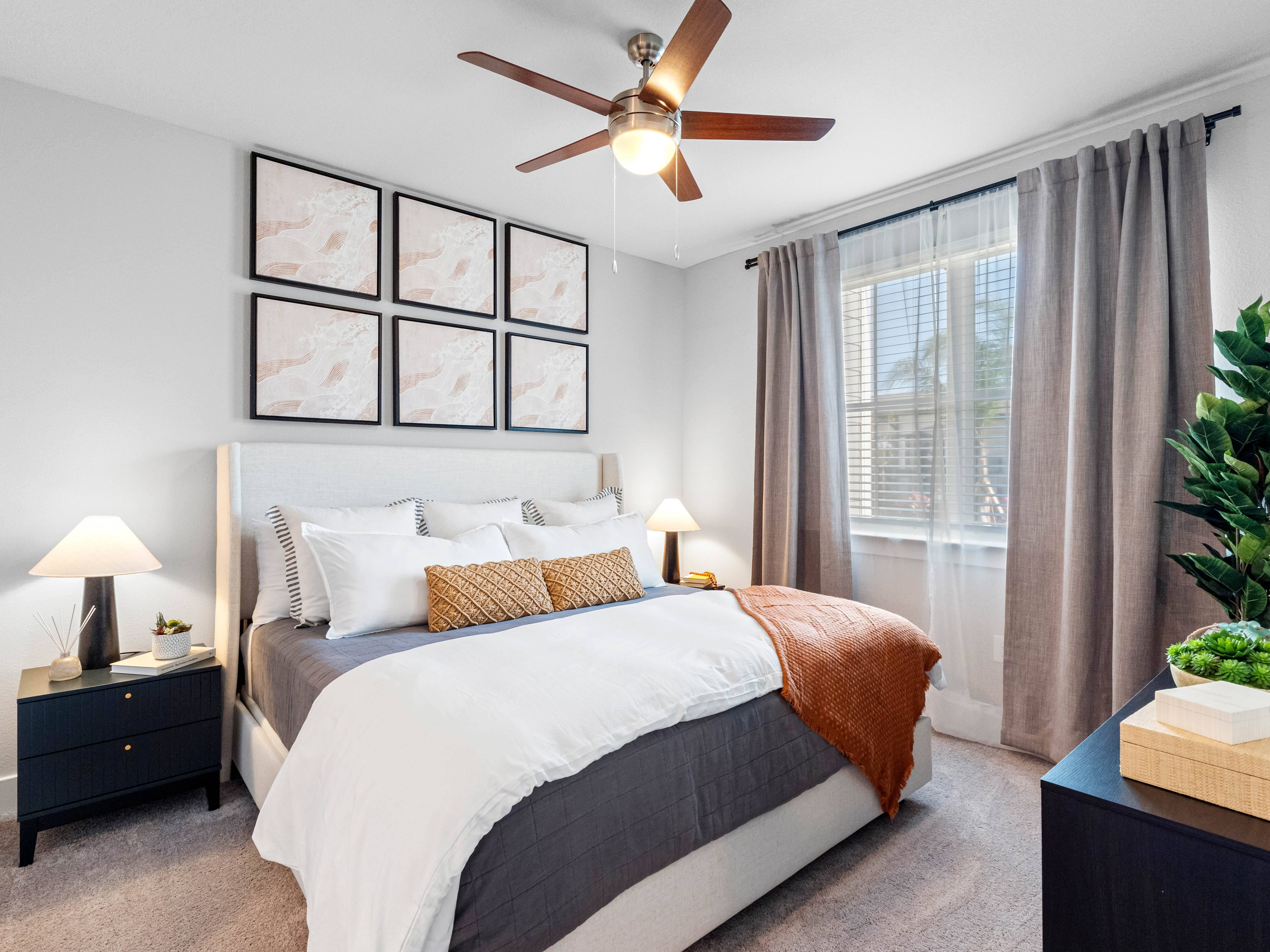 A bedroom with a large bed, a ceiling fan, and a plant on the nightstand.